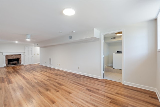 unfurnished living room with a fireplace, washer / clothes dryer, visible vents, light wood-style flooring, and a ceiling fan