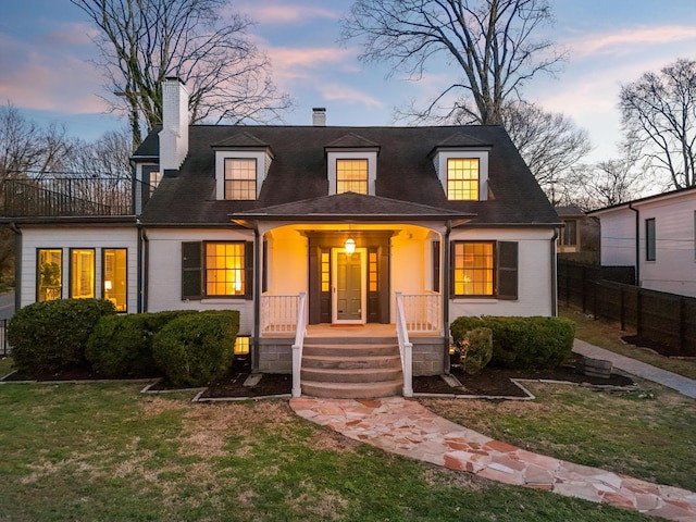 cape cod house featuring a shingled roof, a chimney, covered porch, fence, and a front lawn