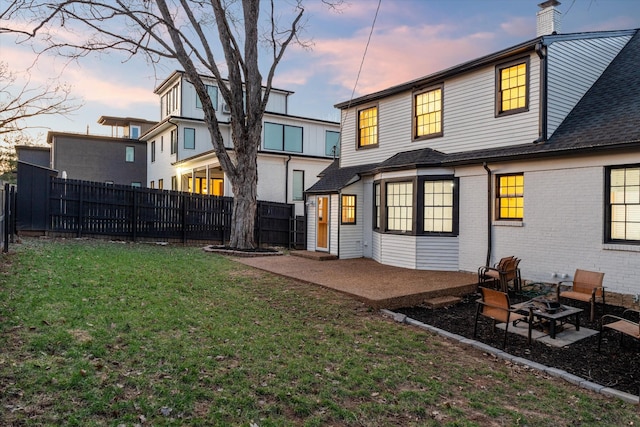 back of property at dusk featuring a fenced backyard, a patio, and a lawn