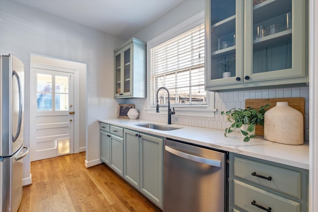 kitchen with light wood-style flooring, glass insert cabinets, appliances with stainless steel finishes, a sink, and backsplash