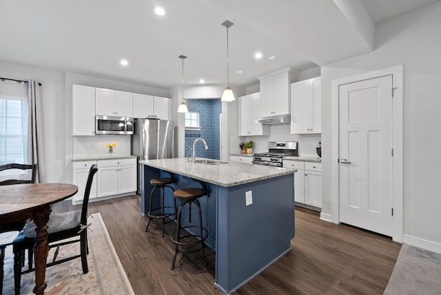 kitchen featuring a breakfast bar, dark wood finished floors, stainless steel appliances, a sink, and under cabinet range hood