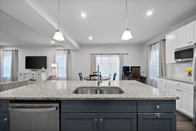 kitchen featuring white cabinets, an island with sink, open floor plan, stainless steel appliances, and a sink