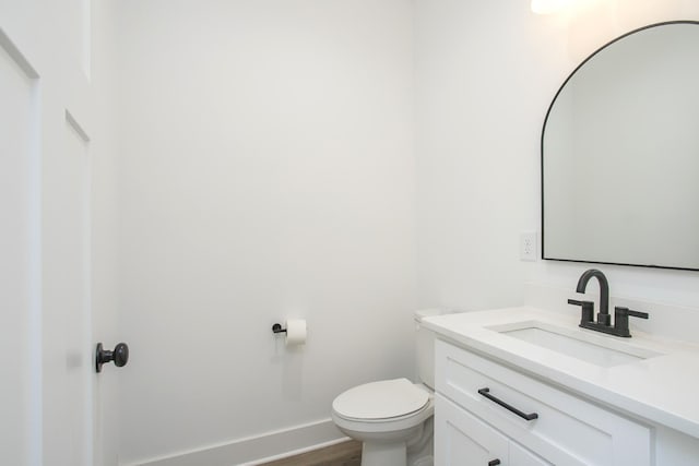 half bath with wood finished floors, vanity, toilet, and baseboards