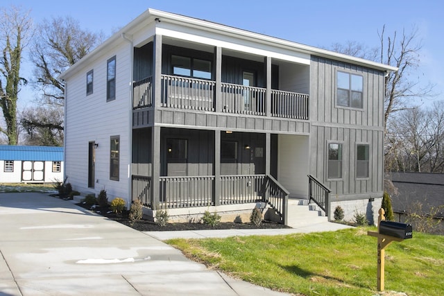 view of property featuring a balcony, covered porch, a front lawn, and board and batten siding