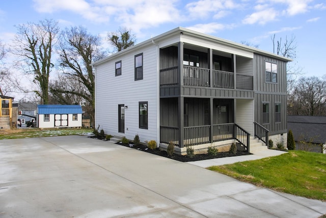 view of front of property featuring driveway, board and batten siding, an outdoor structure, and a balcony