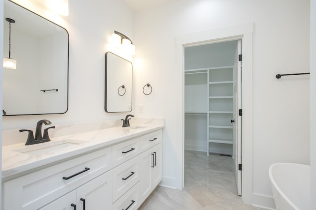 full bathroom featuring double vanity, a freestanding bath, a spacious closet, a sink, and baseboards