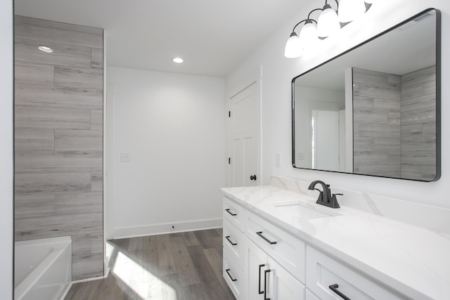 bathroom featuring a bathing tub, recessed lighting, wood finished floors, vanity, and baseboards