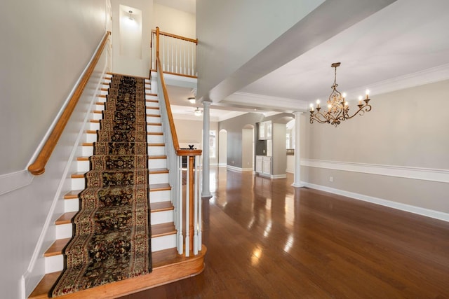 stairway with arched walkways, crown molding, wood finished floors, baseboards, and ceiling fan with notable chandelier