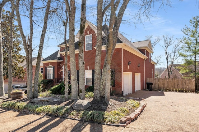 view of property exterior featuring concrete driveway, brick siding, and fence