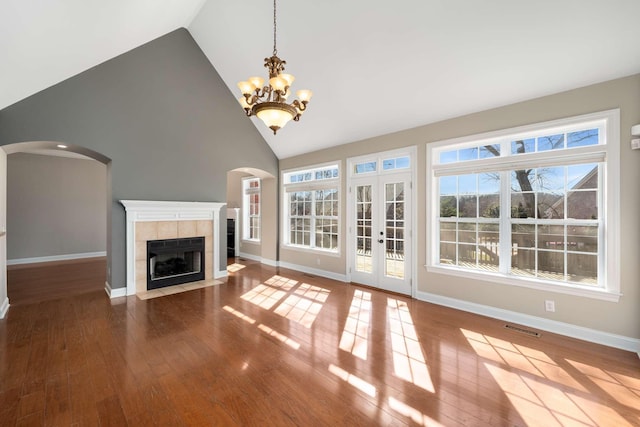 unfurnished living room featuring arched walkways, baseboards, a tiled fireplace, and wood finished floors