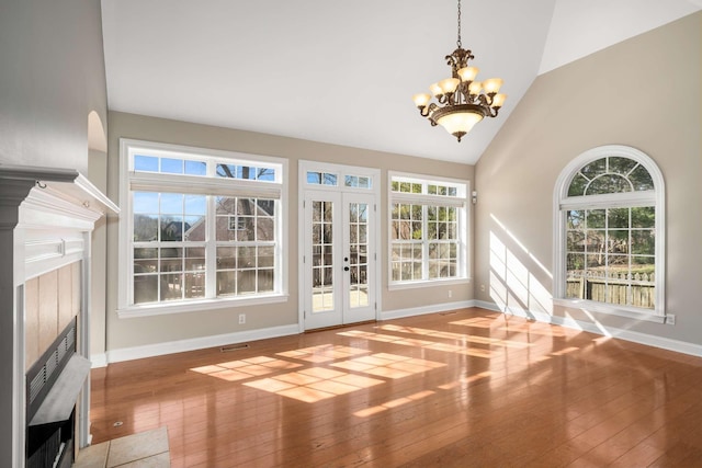 interior space with french doors, a fireplace, a wealth of natural light, an inviting chandelier, and hardwood / wood-style floors