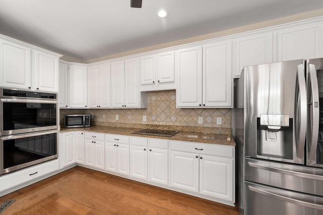 kitchen with appliances with stainless steel finishes, dark stone counters, white cabinetry, and tasteful backsplash