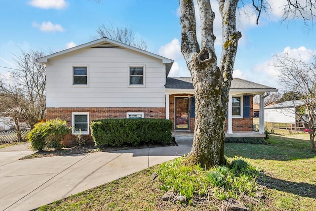 tri-level home featuring brick siding, roof with shingles, a front yard, and fence