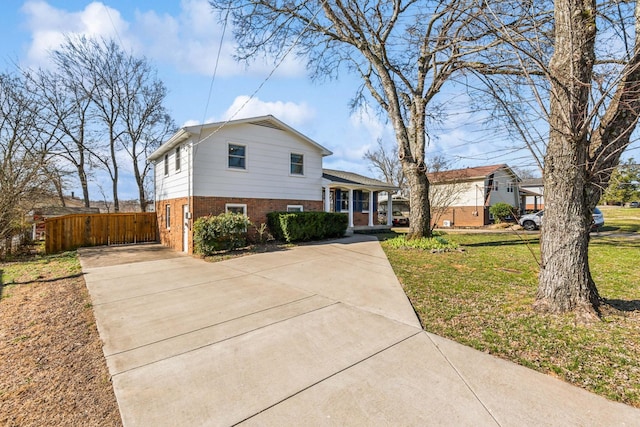 split level home with covered porch, a front yard, fence, and brick siding