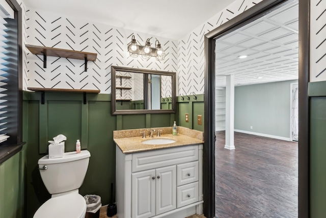 bathroom with wallpapered walls, baseboards, toilet, wood finished floors, and vanity