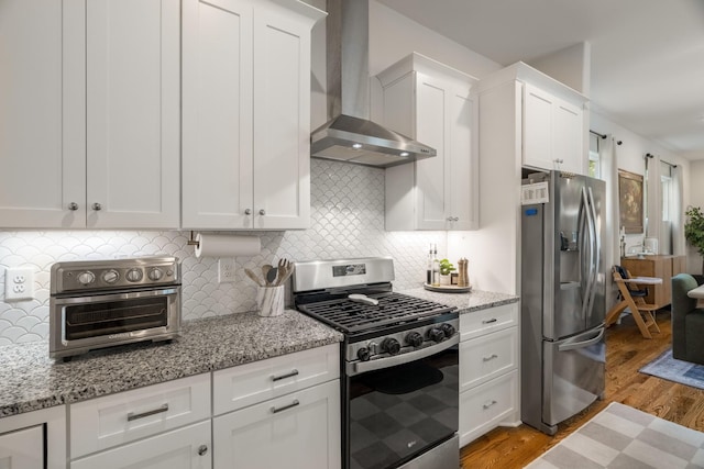 kitchen with a toaster, appliances with stainless steel finishes, white cabinets, wood finished floors, and wall chimney exhaust hood