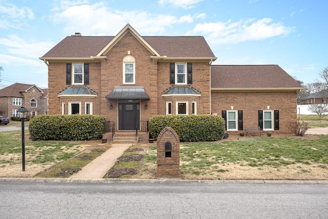 view of front of property with roof with shingles, a front lawn, and brick siding