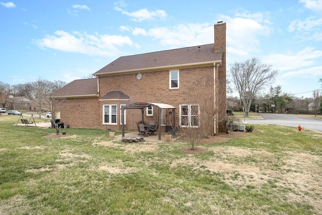 rear view of house with a patio, a yard, a chimney, and brick siding