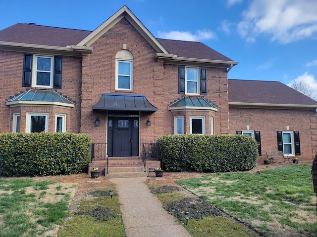 view of front of property with a front yard, a standing seam roof, brick siding, and roof with shingles