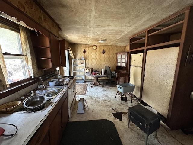 kitchen with open shelves, light countertops, dark brown cabinetry, range, and wallpapered walls