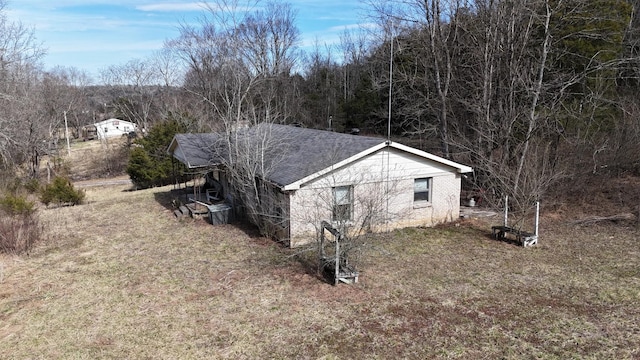 view of side of home with a shingled roof, a wooded view, and brick siding