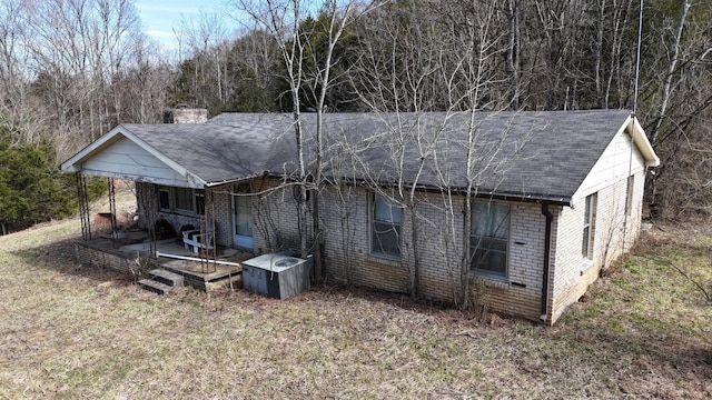 view of front of property featuring brick siding, a shingled roof, a forest view, a front lawn, and a chimney