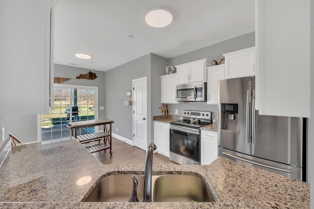 kitchen featuring light stone countertops, appliances with stainless steel finishes, white cabinets, and a sink