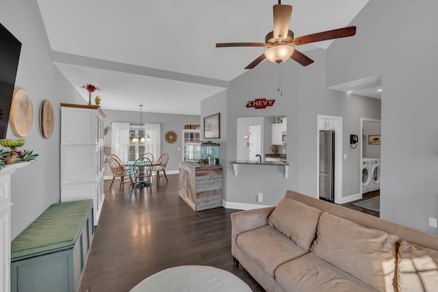 living area with baseboards, dark wood-type flooring, washing machine and clothes dryer, high vaulted ceiling, and ceiling fan with notable chandelier