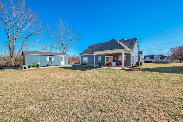 back of house with a patio, an outdoor structure, a ceiling fan, a yard, and roof with shingles