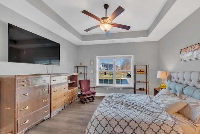 bedroom featuring a tray ceiling, wood finished floors, a ceiling fan, and baseboards