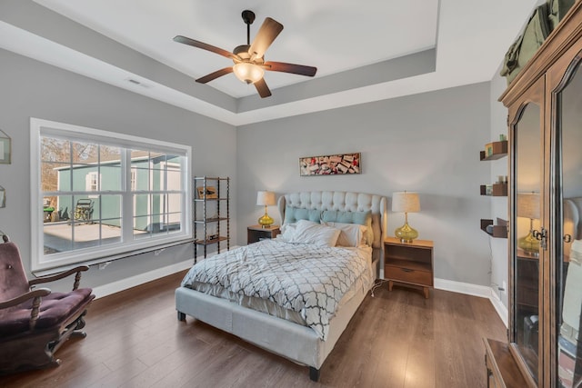 bedroom with ceiling fan, wood finished floors, visible vents, baseboards, and a tray ceiling