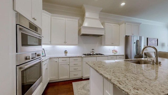 kitchen with a sink, white cabinets, ornamental molding, appliances with stainless steel finishes, and custom range hood