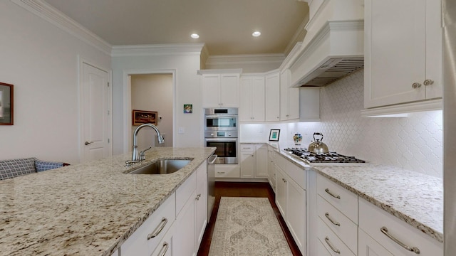 kitchen with light stone counters, a sink, white cabinetry, appliances with stainless steel finishes, and custom exhaust hood