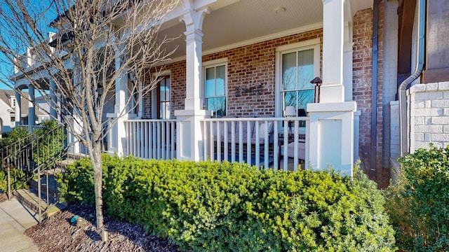 view of exterior entry with brick siding and a porch