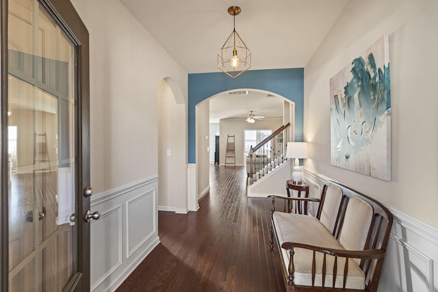 corridor featuring arched walkways, a decorative wall, stairway, wainscoting, and wood finished floors