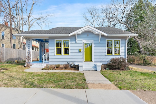 bungalow-style home with a shingled roof, a front yard, and fence