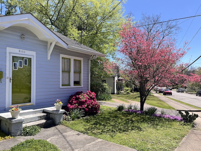 view of side of property with a shingled roof and a lawn