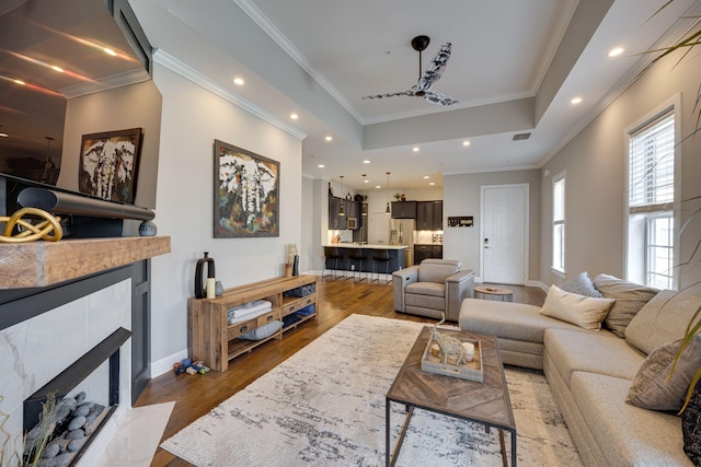 living area with crown molding, recessed lighting, a tiled fireplace, wood finished floors, and baseboards