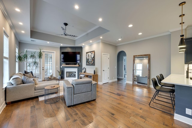 living area with a fireplace, arched walkways, a raised ceiling, and hardwood / wood-style floors