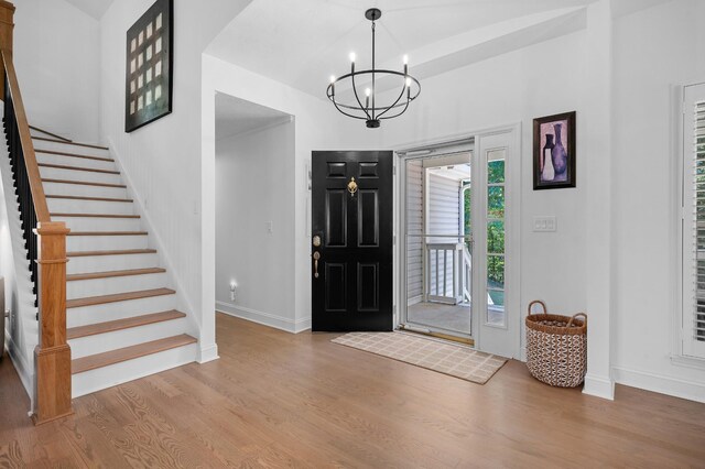 foyer with stairway, a notable chandelier, baseboards, and wood finished floors