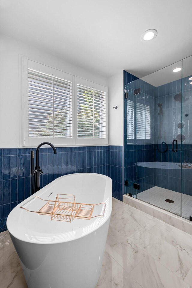 full bathroom featuring tile walls, marble finish floor, a wainscoted wall, and a shower stall