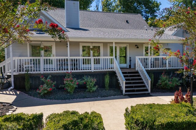 view of front facade featuring a shingled roof, a chimney, a porch, and stairs