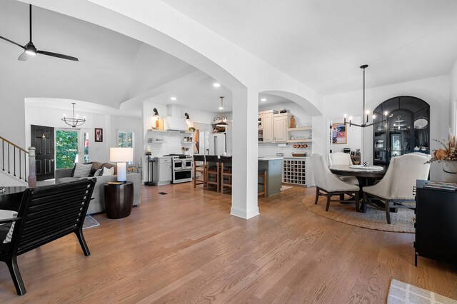 living room featuring arched walkways, recessed lighting, stairway, light wood-style floors, and ceiling fan with notable chandelier