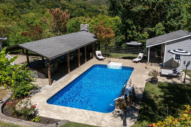 pool with a storage structure, a patio area, fence, and an outbuilding