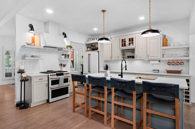 kitchen featuring custom exhaust hood, open shelves, light countertops, high quality appliances, and light wood-type flooring