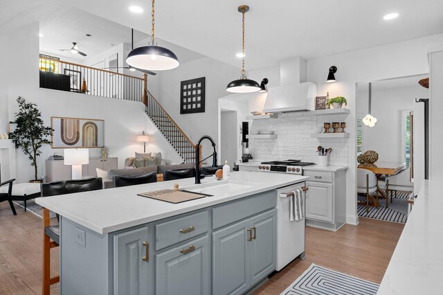 kitchen featuring light wood finished floors, white dishwasher, light countertops, wall chimney range hood, and a sink