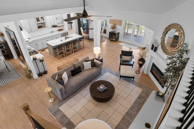 living room with light wood-style floors, a glass covered fireplace, french doors, and a ceiling fan