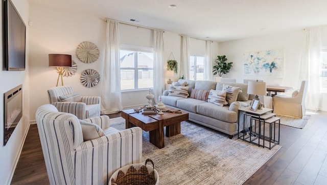 living room featuring dark wood-style flooring, a glass covered fireplace, visible vents, and baseboards