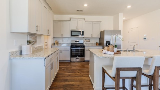 kitchen featuring dark wood-style flooring, recessed lighting, appliances with stainless steel finishes, a sink, and a kitchen bar