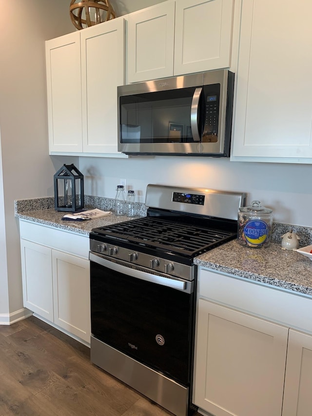 kitchen featuring appliances with stainless steel finishes, light stone countertops, white cabinets, and dark wood-style floors